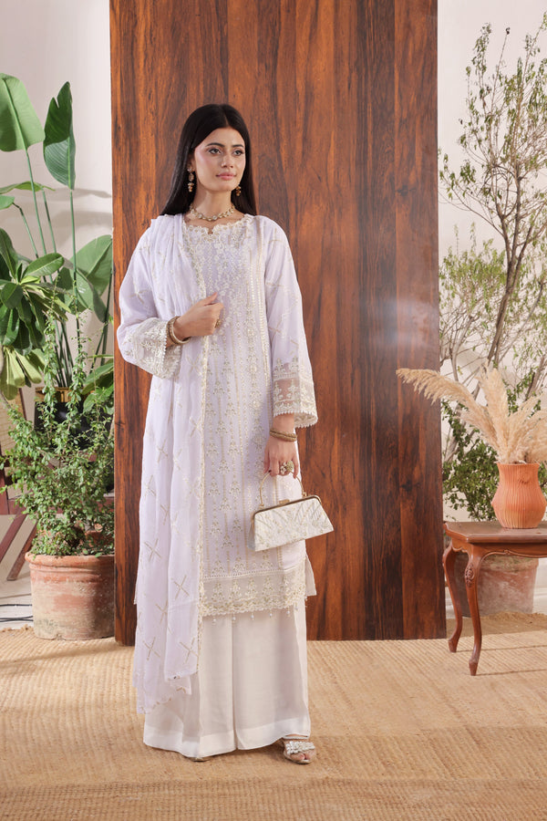 RIWAYAT - Woman in a white traditional outfit standing in a room with plants and wooden elements.