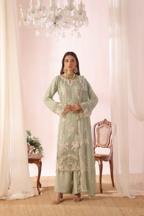 Woman in a light green traditional outfit standing in a decorated room with white curtains and a chandelier.