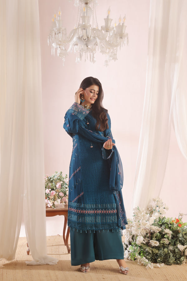 Woman in a blue traditional outfit standing in a decorated room with flowers and a chandelier