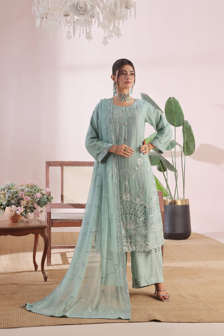 Woman in a light green traditional outfit standing in a room with a chair, table, and plants.